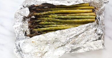 grilled asparagus in foil on a white plate with lemon wedges