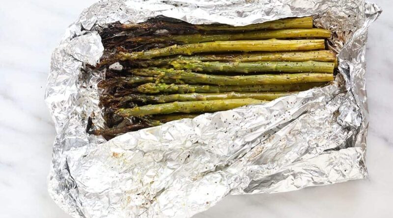 grilled asparagus in foil on a white plate with lemon wedges