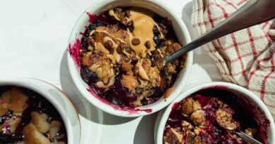 Three small white ramekins filled with baked berry dessert, topped with peanut butter and chocolate chips, with metal spoons and a red-striped cloth nearby.