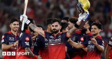 Virat Kohli holds his bat and helmet aloft as his RCB team-mates celebrate winning the IPL