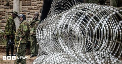  Coils of razor wire are stacked outside a government building as armed security officers stand guard