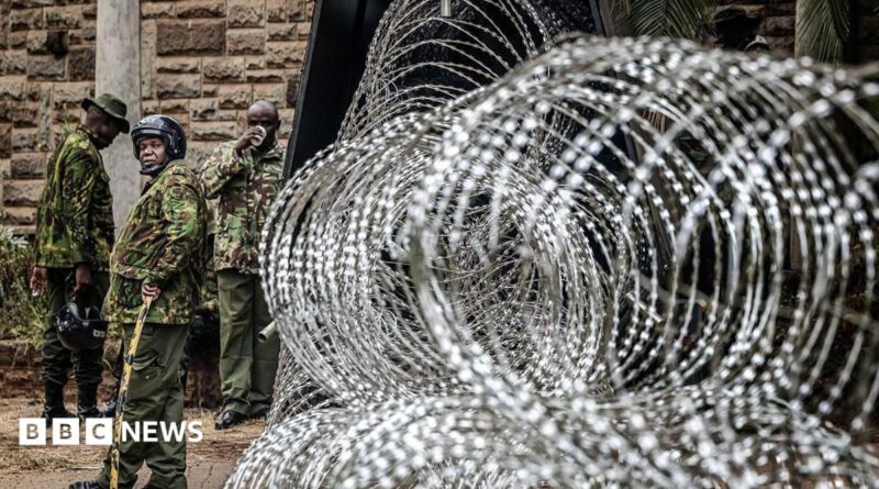 Coils of razor wire are stacked outside a government building as armed security officers stand guard