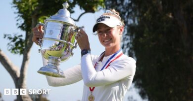 Nelly Korda, wearing a long-sleeved white top and white visor and with a gold medal on a red, white and blue ribbon around her neck, smiles and poses with the silver trophy, holding it up to her right