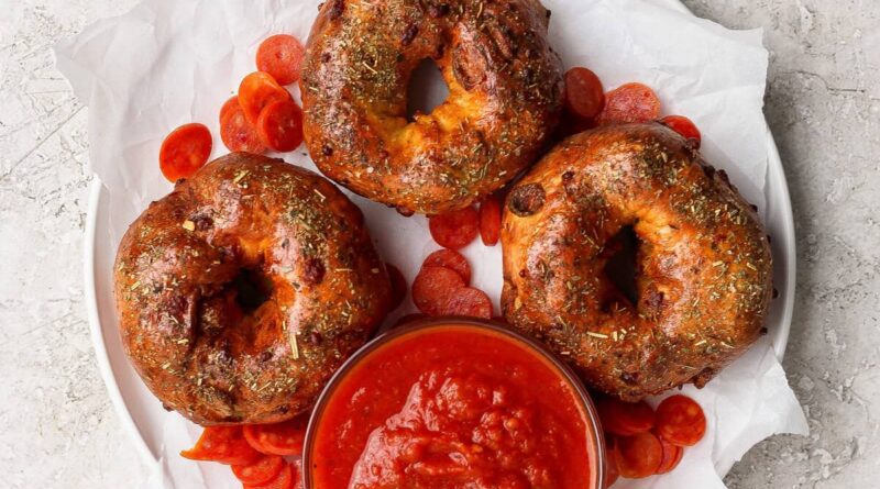 Three pizza protein bagels on parchment paper served with marinara sauce and pepperoni