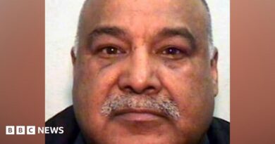 A mugshot of an Asian man in his 60s, with a grey moustache and bald head. He is looking into the camera.
