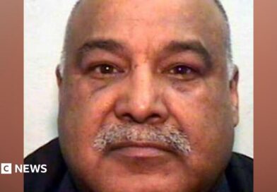 A mugshot of an Asian man in his 60s, with a grey moustache and bald head. He is looking into the camera.
