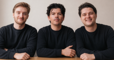 Three caucasian men in black long-sleeved crewneck shirts sit at a desk against a beige background.