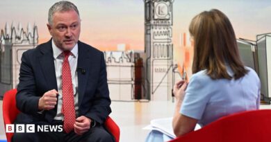 Housing, Communities and Local Government Secretary Steve Reed appearing on the Sunday with Laura Kuenssberg, with presenter Victoria Derbyshire standing in. The pair sit on red bucket chairs. Reed wears a black suit with a white shirt and a red tie. Derbyshire is wearing a pastel blue dress with short sleeves. She has shoulder length, dark blonde hair.