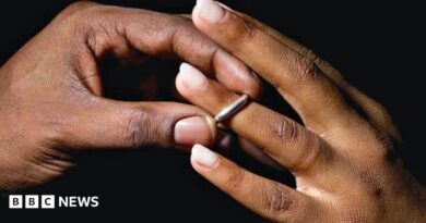 A man places a silver wedding band onto a young woman's ring finger.