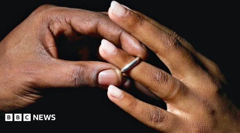 A man places a silver wedding band onto a young woman's ring finger.