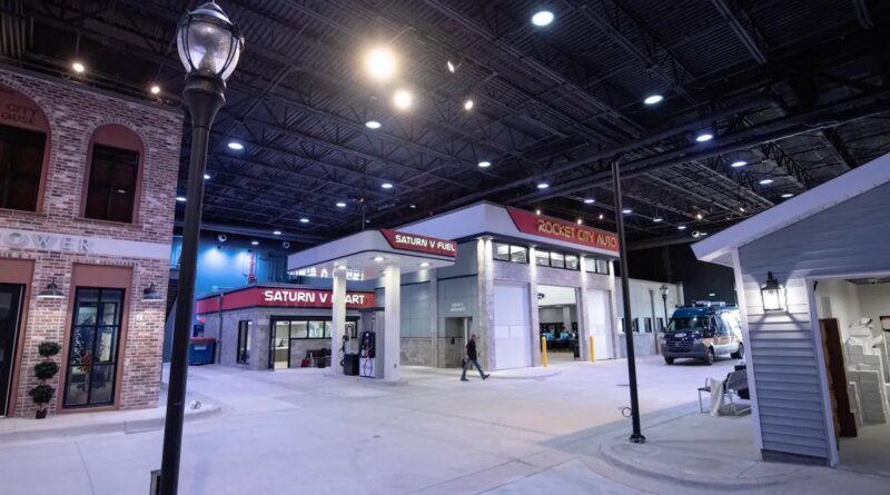 a screenshot from the FBI's Kinetic Cyber Range video, showing the FBI's model town cross walk, including a business center, and a light post, inside a large warehouse space.