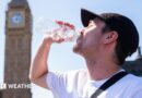 A man drinks from a water bottle with a sunny sky overhead and a blurred view of the Westminster skyline in the background