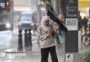 A woman tries to reverse her inside out umbrella in rainy conditions 