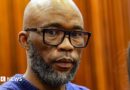 A head and shoulders picture of Cat Matlala in court - he is wearing a blue jumper, the neckline of which can just be seen at the bottom of the picture.