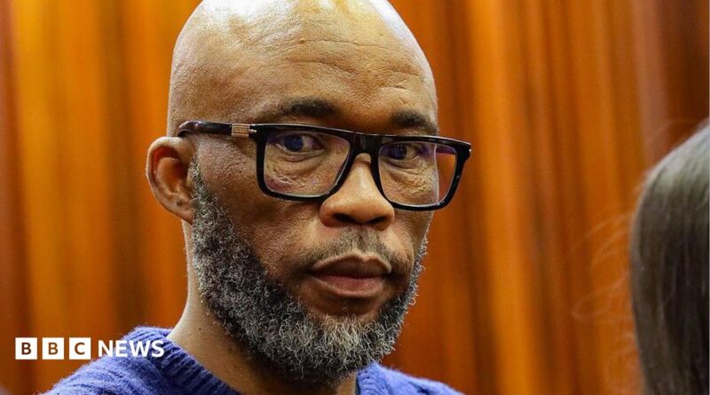 A head and shoulders picture of Cat Matlala in court - he is wearing a blue jumper, the neckline of which can just be seen at the bottom of the picture.