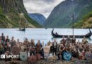 Norway players in Viking dress and with weapons and shields pose in front of a fjord with Viking boats
