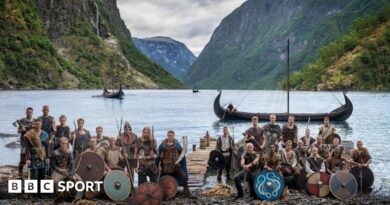 Norway players in Viking dress and with weapons and shields pose in front of a fjord with Viking boats