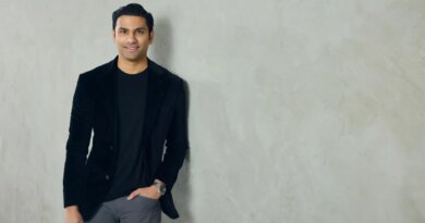 A well-dressed man leans against a neutral colored wall