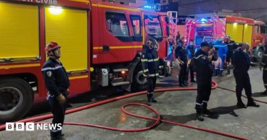 Firefighters in blue uniforms stand in front of fire trucks