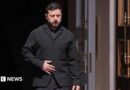 Zelensky, wearing a dark suit, walking through a doorway
