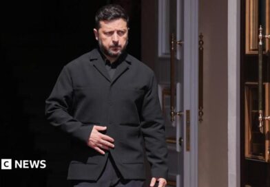 Zelensky, wearing a dark suit, walking through a doorway