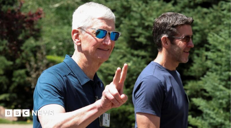 Apple CEO Tim Cook walking outside, throwing up 'peace' fingers, wearing a blue polo shirt and reflective sunglasses. John Ternus, who will replace Cook as CEO later this year, walks beside him, wearing a blue t-shirt and sunglasses.