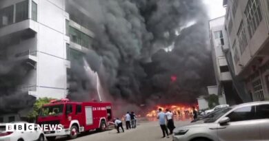 Plumes of black smoke and flames can be seen as a fire truck sprays a burning building with water