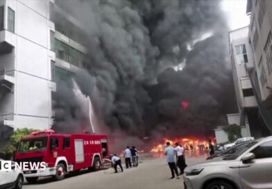 Plumes of black smoke and flames can be seen as a fire truck sprays a burning building with water