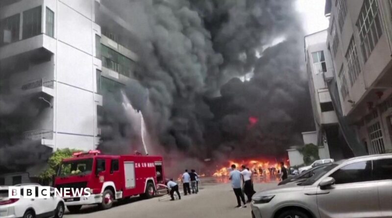 Plumes of black smoke and flames can be seen as a fire truck sprays a burning building with water