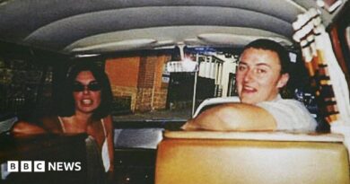 Joanne Lees and Peter Falconio sitting in a van, turning to face the person taking the photo, who is in the back seat. Lees has dark, shoulder-length hair and is wearing black sunglasses. Falconio is smiling and has short dark hair and a white t-shirt on.