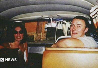 Joanne Lees and Peter Falconio sitting in a van, turning to face the person taking the photo, who is in the back seat. Lees has dark, shoulder-length hair and is wearing black sunglasses. Falconio is smiling and has short dark hair and a white t-shirt on.