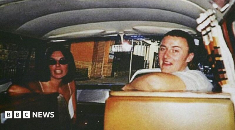 Joanne Lees and Peter Falconio sitting in a van, turning to face the person taking the photo, who is in the back seat. Lees has dark, shoulder-length hair and is wearing black sunglasses. Falconio is smiling and has short dark hair and a white t-shirt on.