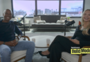TechCrunch Build Mode podcast host Isabelle Johannessen sits across from venture capitalist Charles Hudson in a bright podcast studio. Both are smiling toward the camera, seated in armchairs with microphones positioned between them. A coffee table with two mugs sits in the foreground, while large windows behind them overlook the San Francisco skyline. The TechCrunch Build Mode logo appears in the bottom-right corner.