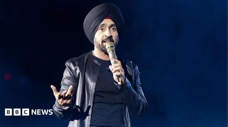 Diljit Dosanjh kicks off his Aura World Tour at BC Place on April 23, 2026, in Vancouver, British Columbia, Canada. He is wearing a black jacket over a black t-shirt and sporting a black turban, as he speaks on a microphone from the stage.