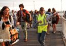 A volunteer gives indication to holidaymakers from Lege-Cap-Ferret upon their arrival in Arcachon by boat during an evacuation operation of the entire Cap-Ferret peninsula, in southwestern France, on July 24, 2026 whilst a wildfire is spreading across the area