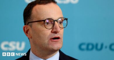 Jens Spahn speaks with German media during a party meeting, he is wearing a black suit and black glasses.