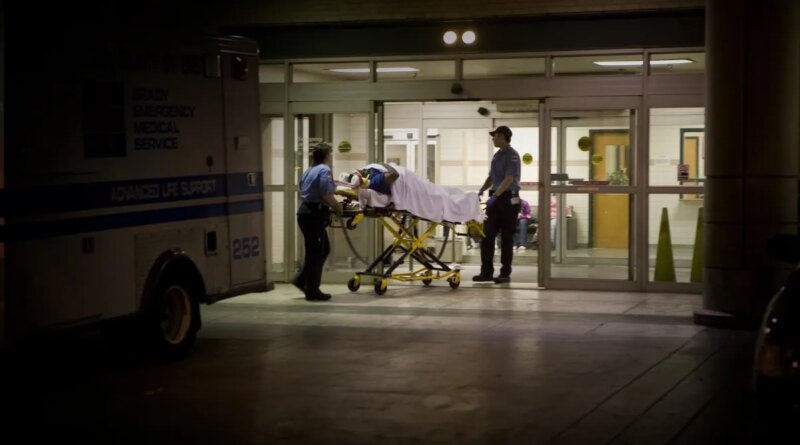 a person wheeled in on an ambulance stretcher outside of a U.S. emergency room at night