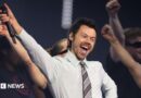 Harry Styles, who has styled short brown hair, performing in a white shirt and grey tie on stage at the BRIT awards earlier this year