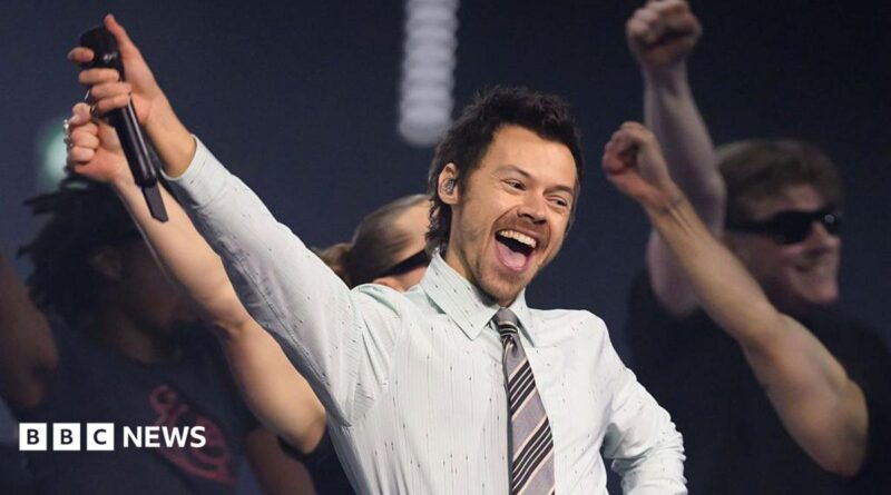 Harry Styles, who has styled short brown hair, performing in a white shirt and grey tie on stage at the BRIT awards earlier this year