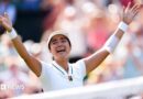 Filipina tennis player Alexandra Eala raises his arms after a Wimbledon match, net in front of her and a blurred image of the crowd in the background.