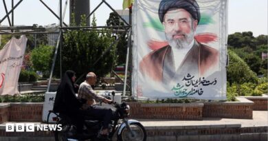 A man and a woman on a motorcycle pass a large portrait of Supreme Leader Ayatollah Mojtaba Khamenei on a street in Tehran.