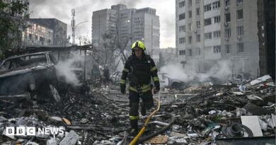 Sarah Rainsford in a brown shirt with short sleeves in front of rubble in Kyiv