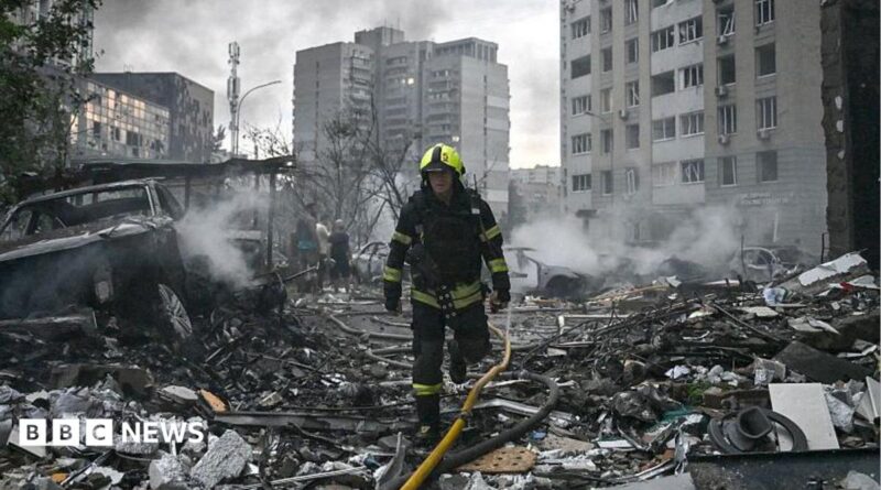 Sarah Rainsford in a brown shirt with short sleeves in front of rubble in Kyiv