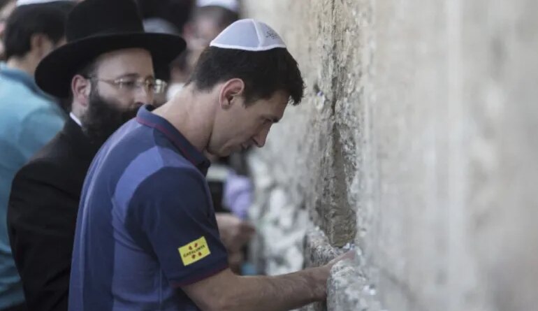 FC Barcelona football player Lionel Messi (R) puts a paper with wishes in a crack in the Western Wall, Judaism's holiest site, in Jerusalem, August 4, 2013. The club is on a two-day visit to Israel and the West Bank. AFP PHOTO/OLIVER WEIKEN-POOL (Photo by OLIVER WEIKEN / POOL / AFP)