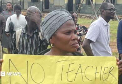 A woman holds up a banner at a protest at a school.