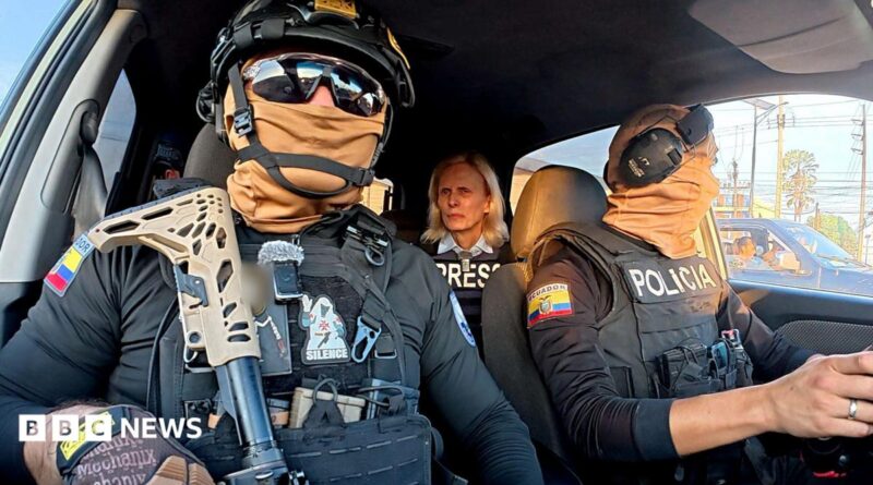 Two Ecuadoran police officers in dark sunglasses, helmets and balaclavas - which entirely obscure their faces - sit in a car in front of the BBC's Orla Guerin, wearing a flak jacket with the word "PRESS" on it.