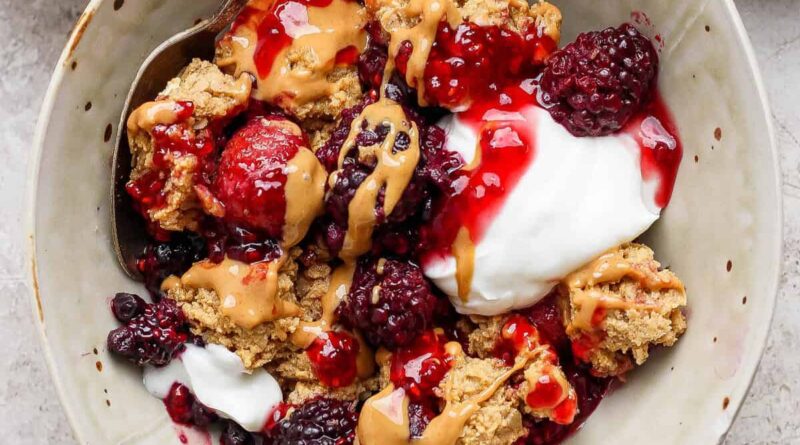 protein berry crumble served in a bowl with yogurt and peanut butter drizzle