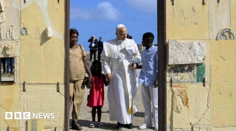 Pope Leo holds hands with a girl wearing a red dress and a man in blue shirt and white trousers. A women in a beige outfit stands alongside them at a doorway. Behind them are blue skies and men dressed in black