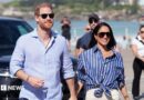 Prince Harry, Duke of Sussex, and his wife Meghan, the Duchess of Sussex walking hand in hand, wearing blue shirts and sunglasses.