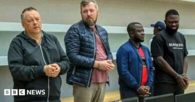 Four handcuffed men standing in front of a row of confiscated laptops. Lev Lakshtanov, Igor Ratchin, Amor Carlos Tomé and Francisco Oliveira (left to right)